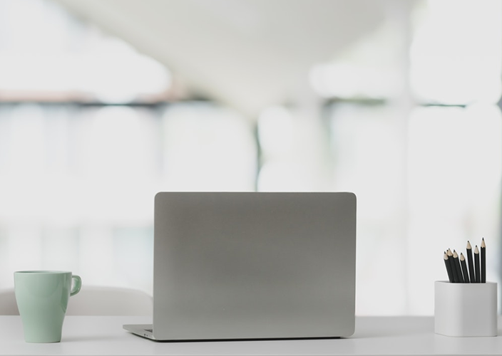 A desk with a laptop, mug, and container of pencils on it.