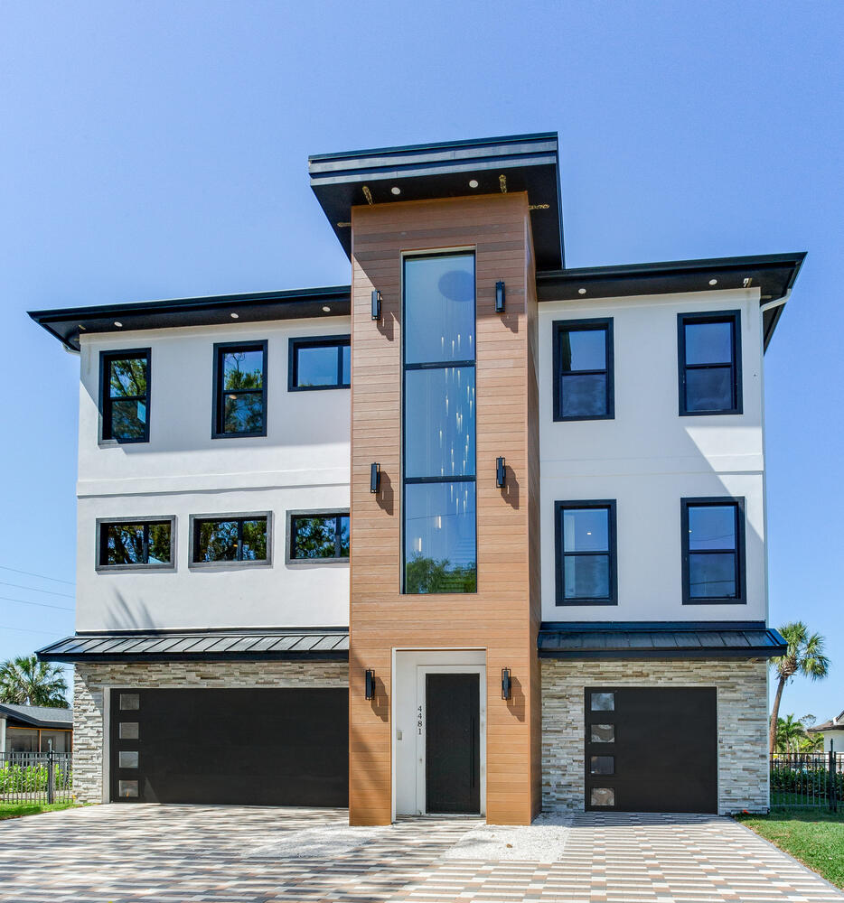 Contemporary multi-story custom home exterior with a bold vertical entry feature, large windows, garage parking, and modern coastal architecture.