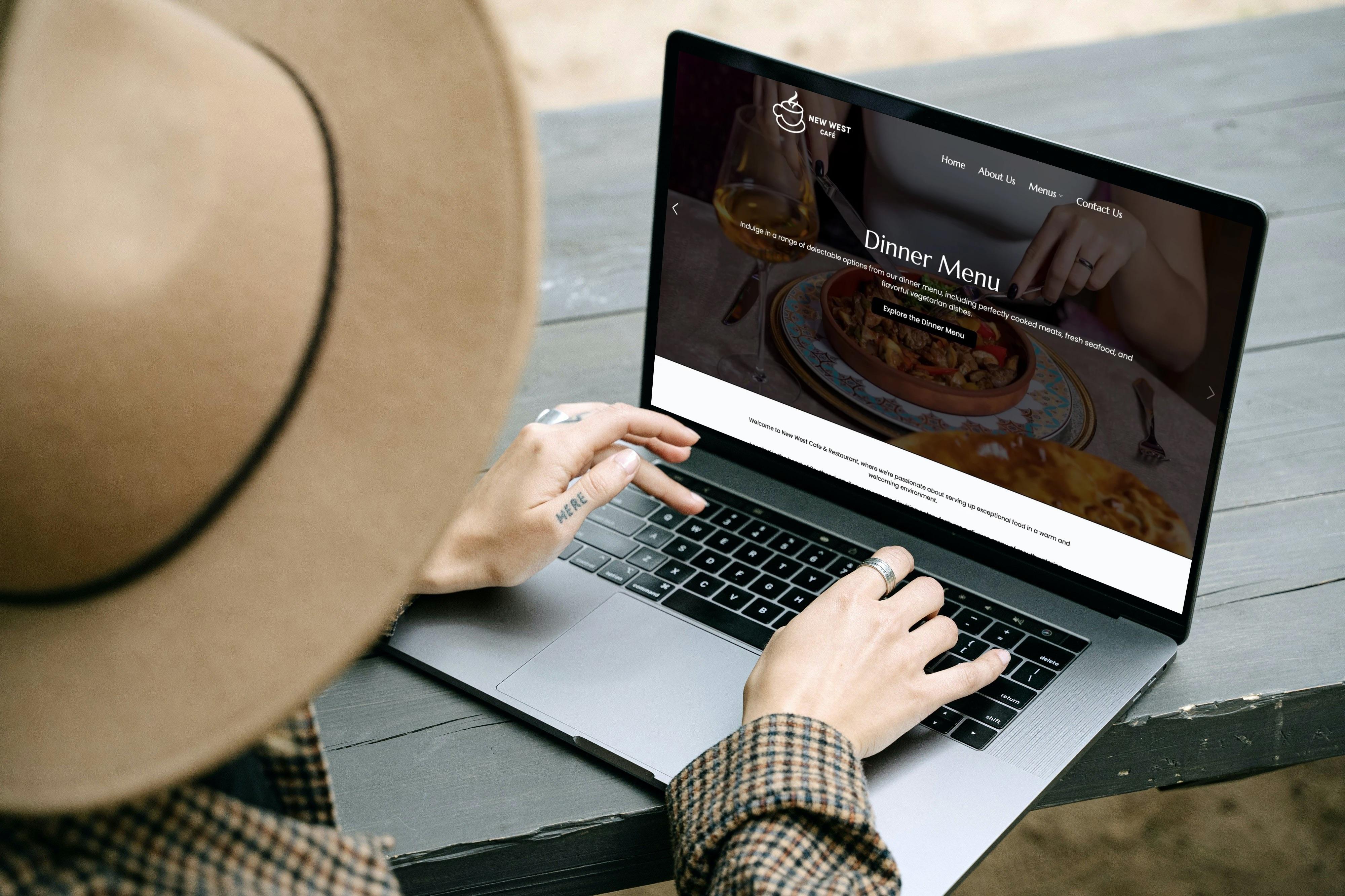 Web design mockup for New West Caf&eacute; restaurant website displayed on a MacBook laptop, featuring a dark hero section with dinner menu slider and elegant typography.