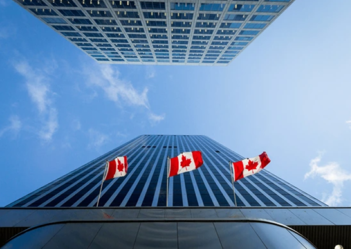 Bottom-up view of a skyscraper with three billowing Canadian flags near the bottom.