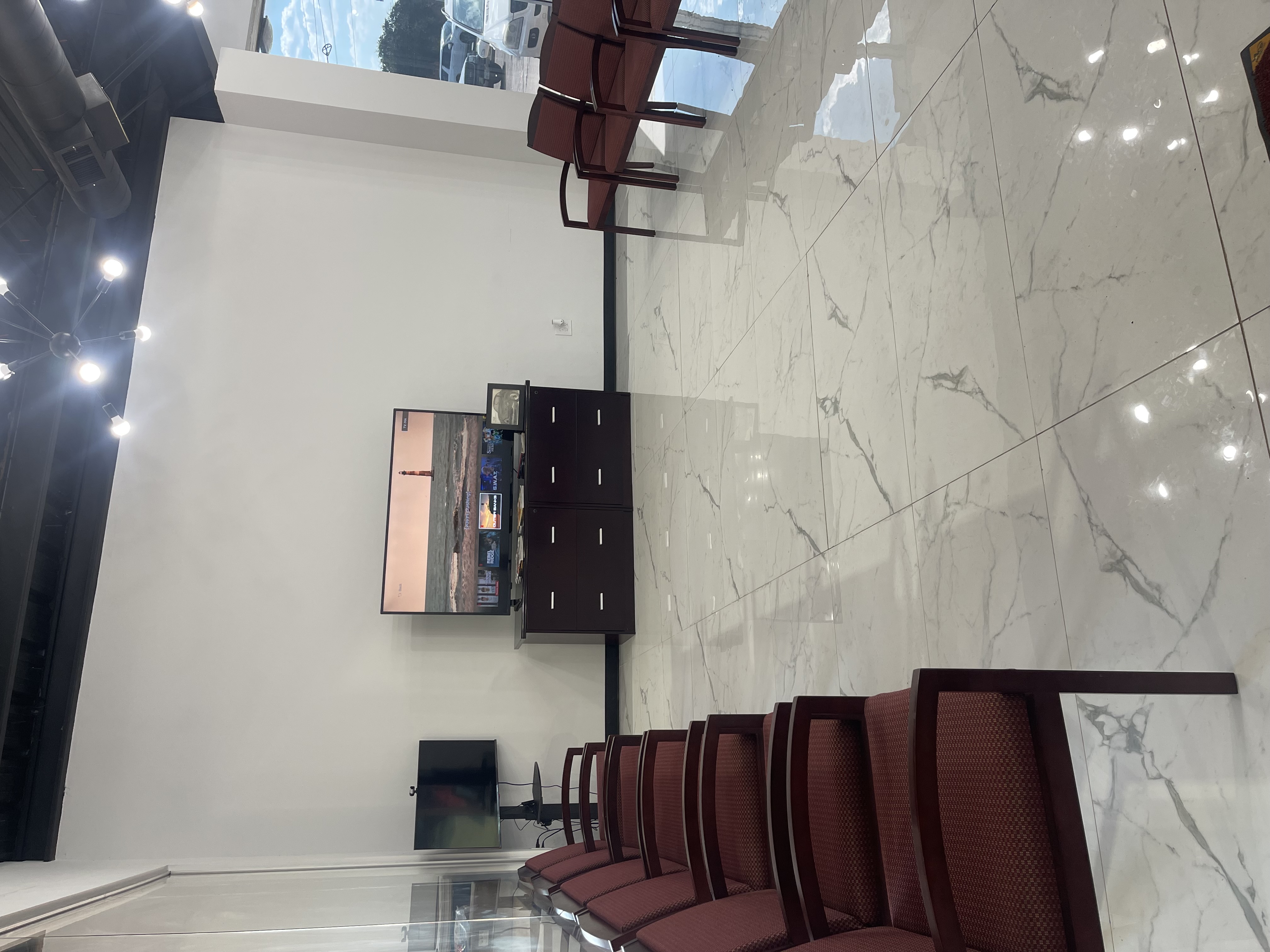 Spacious customer waiting area inside Yes! Automotive in Houston, Texas, featuring a wall-mounted flat-screen television, dark wood cabinets, and comfortable armchair seating on marble-look tile floors.