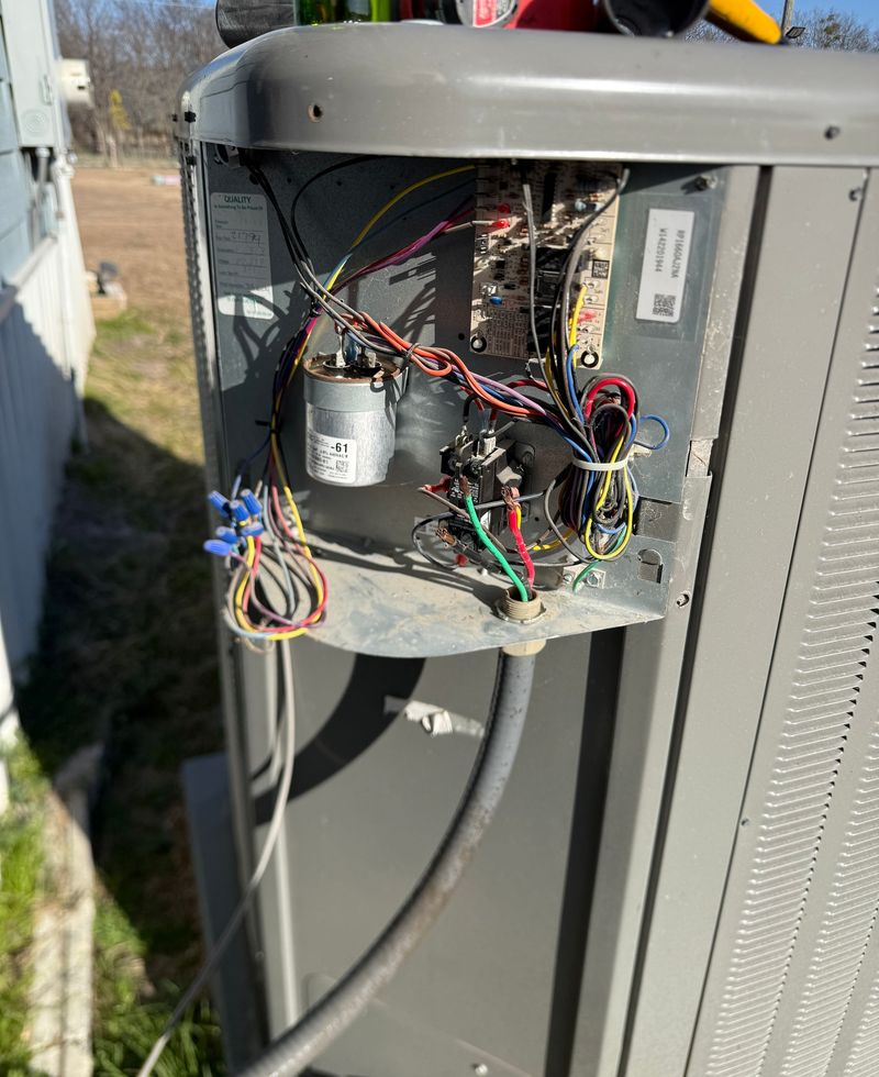Open outdoor HVAC unit showing internal wiring, capacitor, and electrical components during repair or inspection. Technician exposes control panel, highlighting connections, wear, and system condition for troubleshooting and maintenance work.