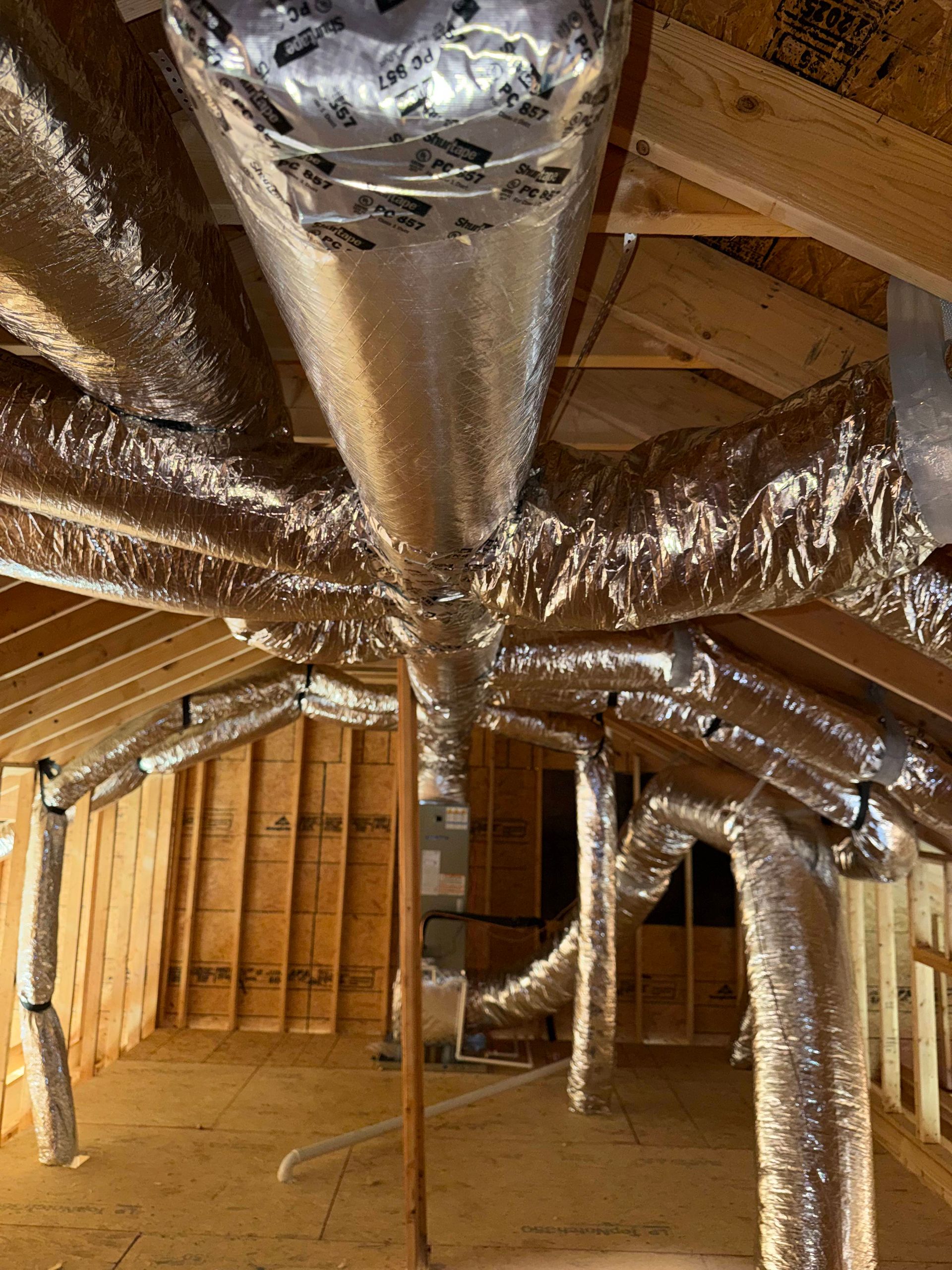 Attic HVAC ductwork network featuring multiple insulated flexible ducts branching through exposed wo 