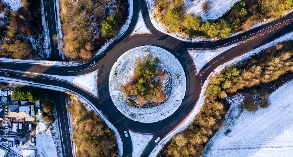 Overhead view of snow-covered roundabout surrounded by autumn forest with connecting roads.