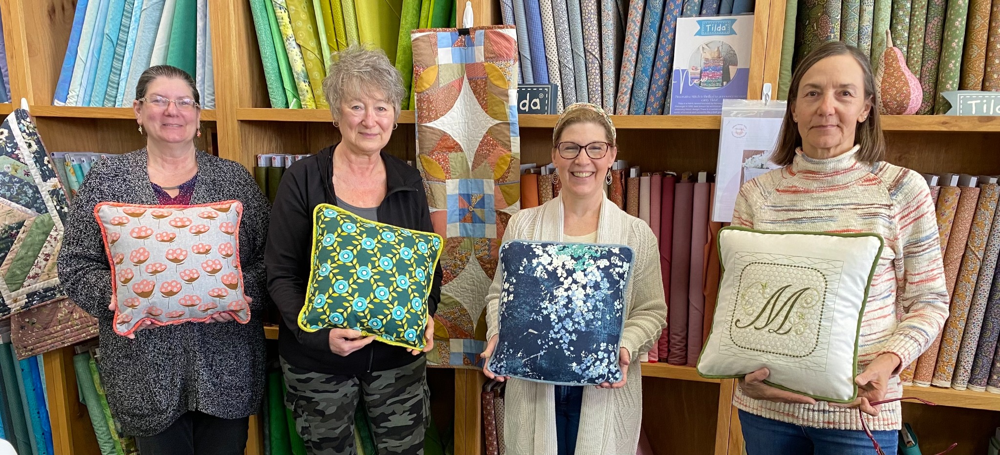 Students proudly display their finished decorative throw pillows after a Decorative Stitch class. This hands-on sewing workshop featured decorative stitching, piping, quilting techniques, and personalized pillow designs.