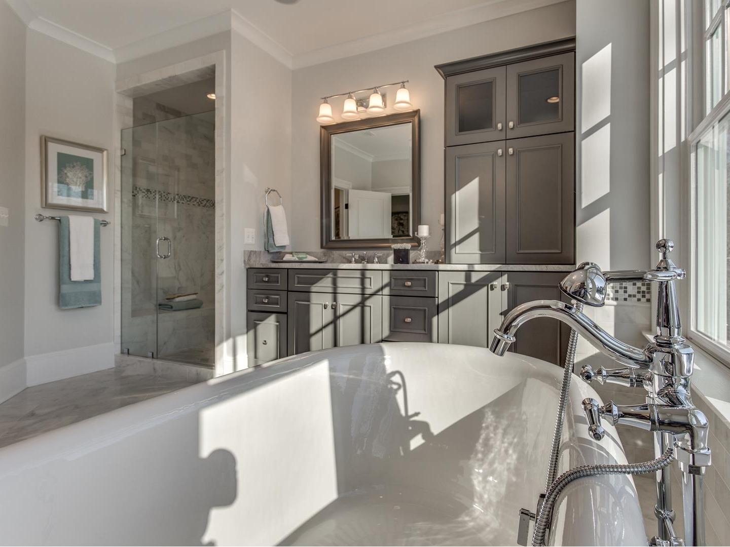 A view from the tub into a design featuring painted grey bathroom vanity cabinets.