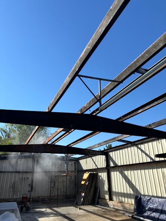 A construction worker is cleaning the steel beams of a building under construction with a spray wash 