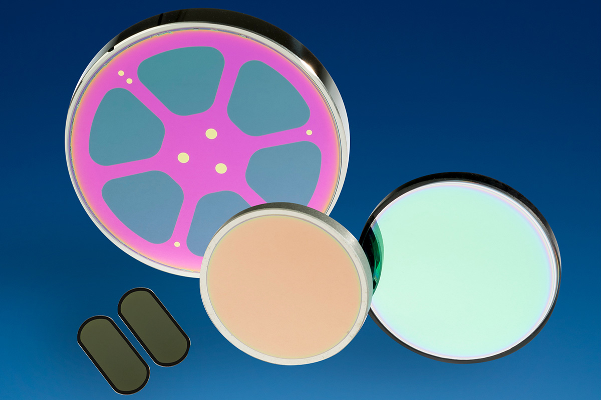 Collection of custom optical components showcasing DSI's comprehensive coating capabilities, including patterned photolithography coatings (pink/teal wafer), bandpass filters (various colored circular optics), and specialized thin film coatings. Products demonstrate UV through VLWIR spectral range coverage (up to 22 μm) for aerospace, defense, biomedical imaging, and scientific research applications.