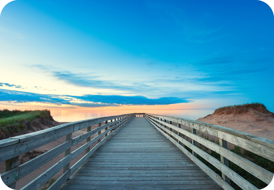 A beach boardwalk leading towards calm waters at sunset in Prince Edward Island National Park.