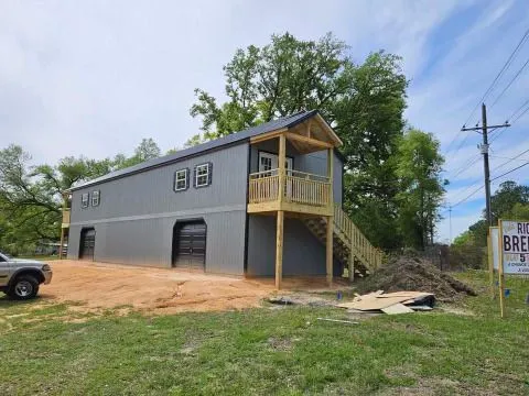 Large two-story portable garage with upper-level balcony, staircase, and dual garage doors. Built for vehicle storage, workshop use, or expanded residential functionality with attractive exterior finishes.