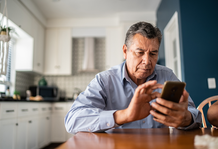 An older gentlemen on his phone at the kitchen table.