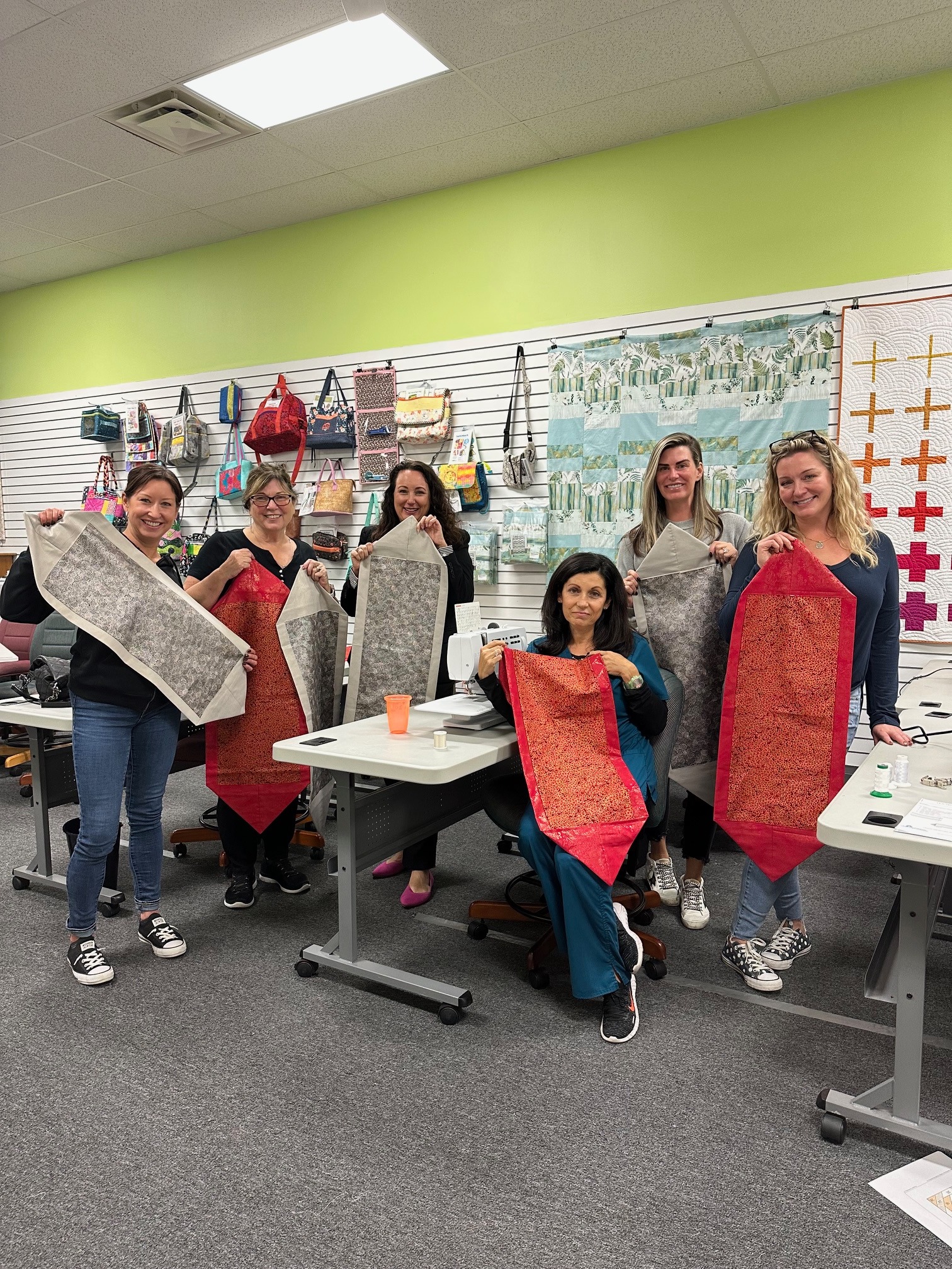 Students proudly showcase their completed table runner projects after a Decorative Stitch class. This hands-on quilting workshop focused on decorative stitching, precision piecing, and creating beautiful handmade home décor.