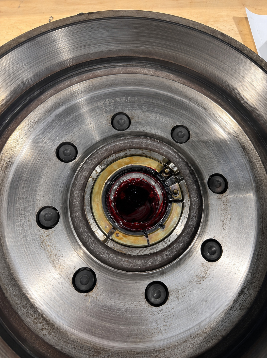 Close-up of a large circular brake rotor and hub assembly showing machined metal surfaces, wheel studs, central bearing area, grease, and wear patterns during inspection or repair work inside workshop.
