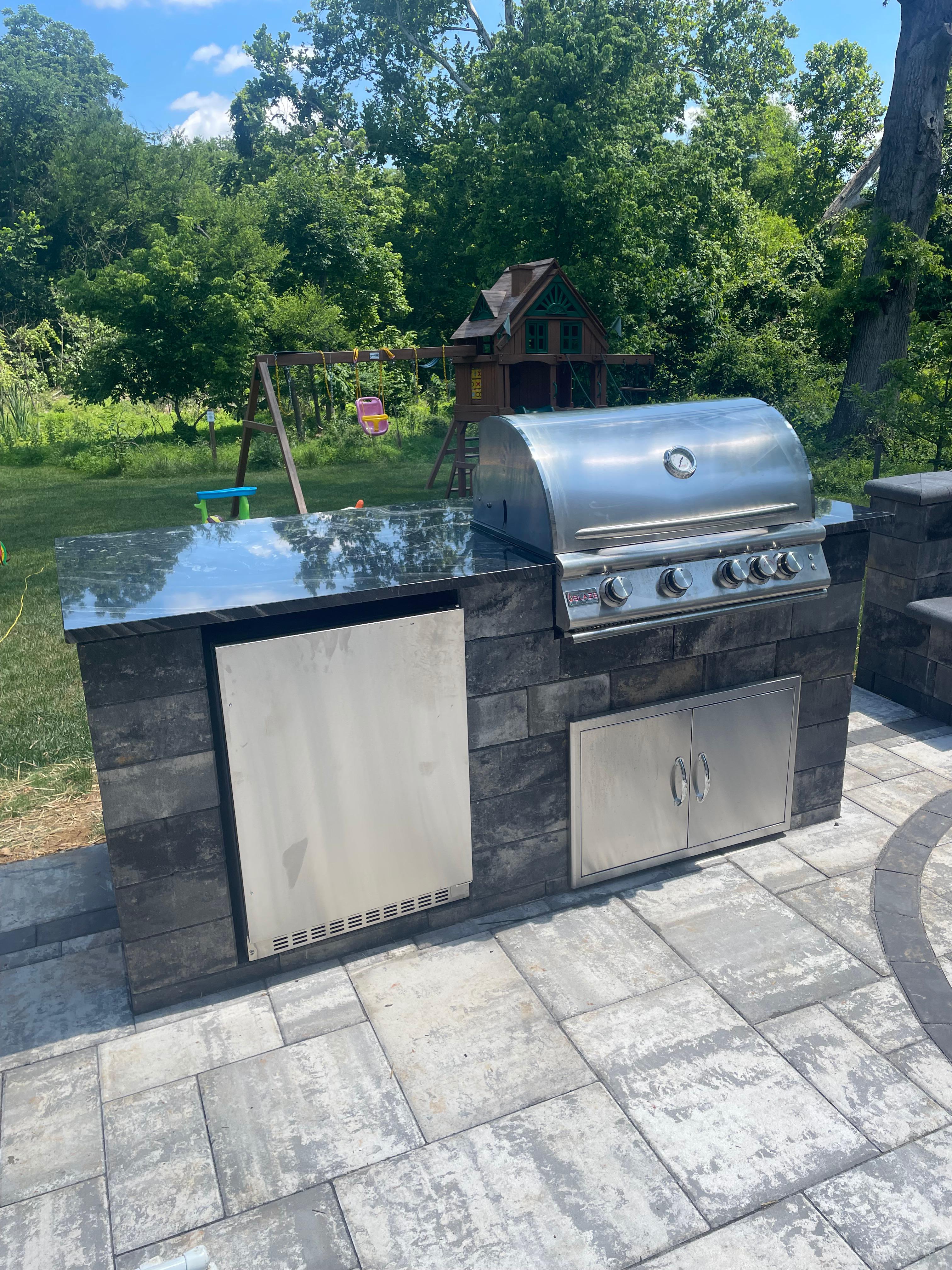 Outdoor stone kitchen with built in grill and mini fridge.