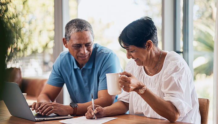 A couple filling out paperwork at their dining table.