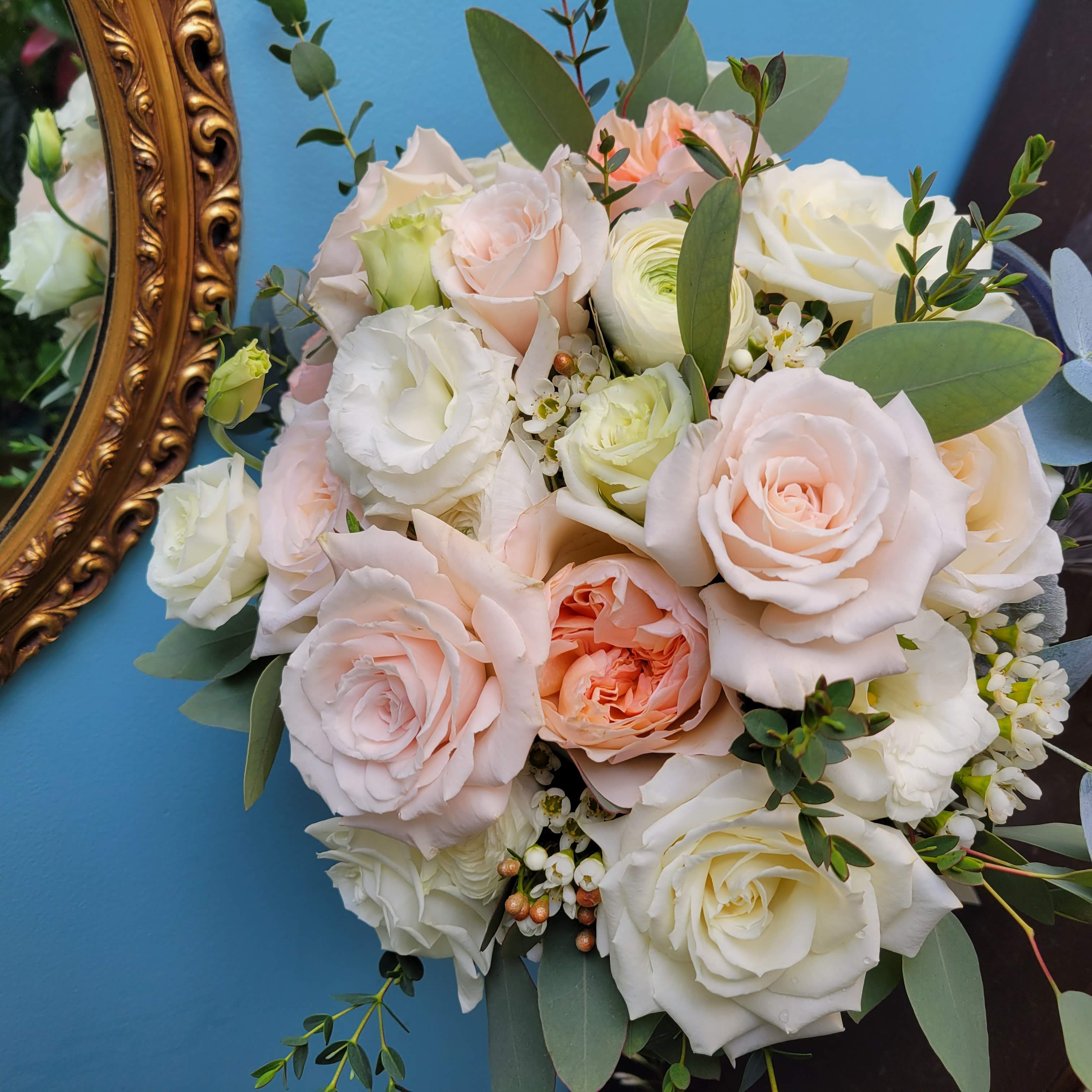 Compact Bridal bouquet with sweetheart roses, ranunculus, lisianthus, eucalyptus, and dusty miller in a color palette of blush, white, cream, and green.