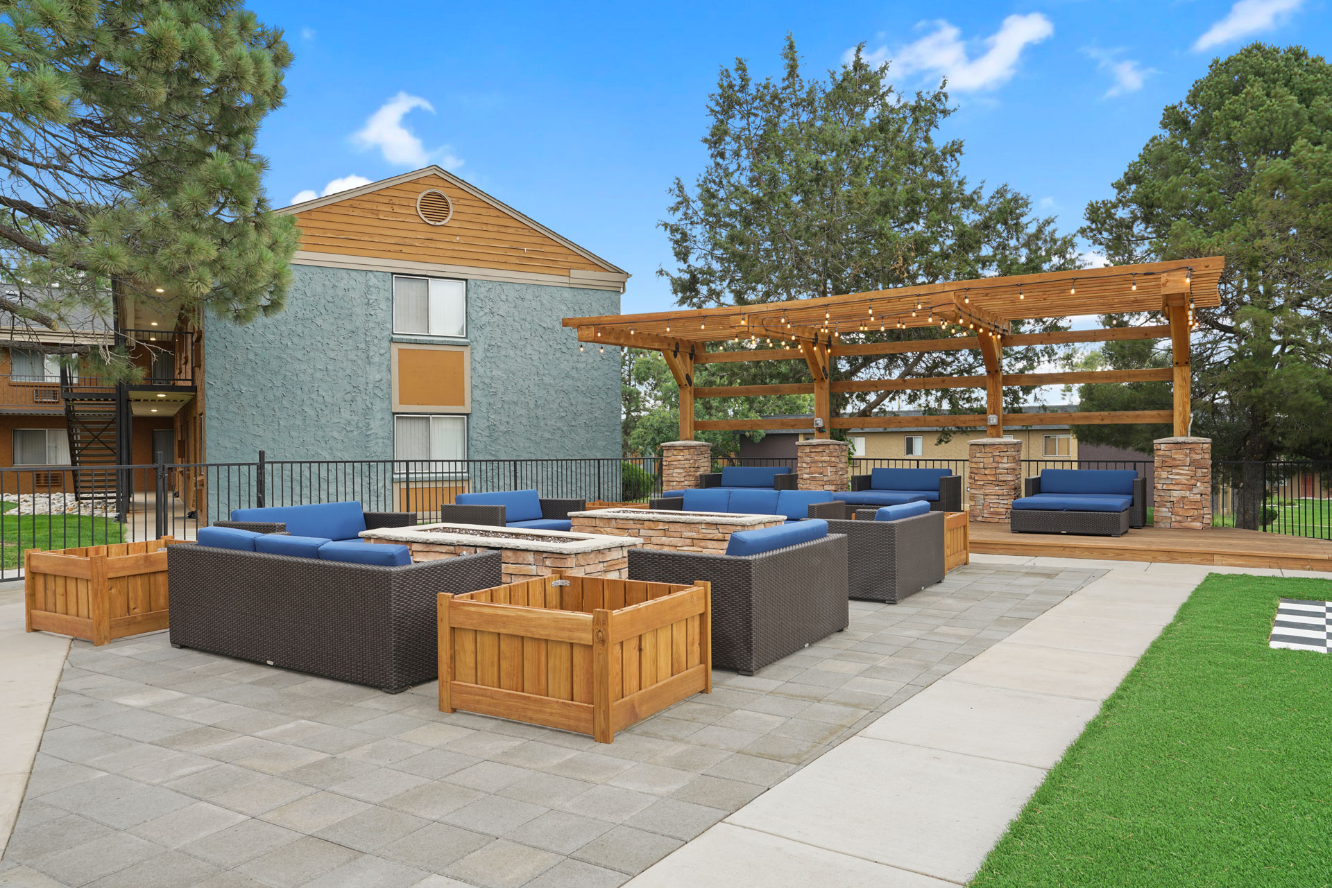 A patio with a wooden pergola and grey cushioned seating.