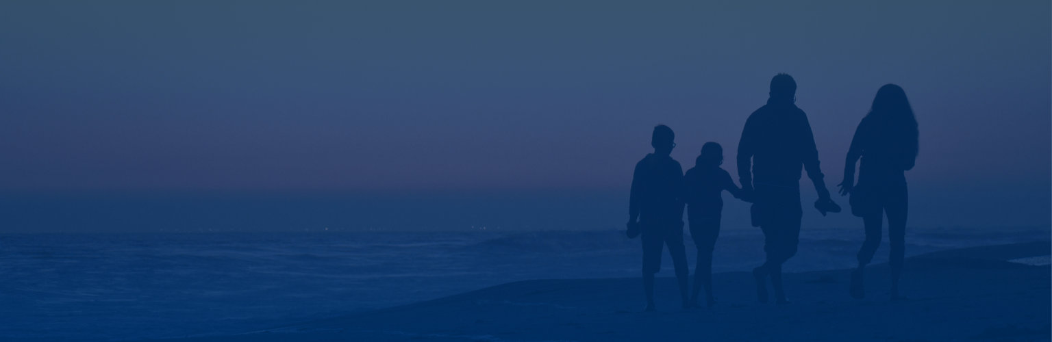 Silhouettes of a family of four walking side by side along the beach shore at sunset.