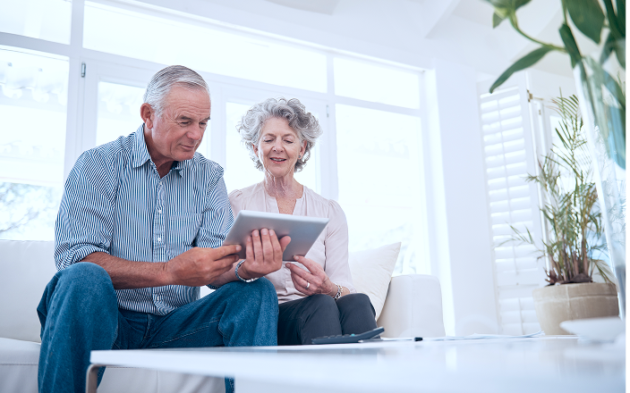 A couple sitting on the couch and looking at their tablet.