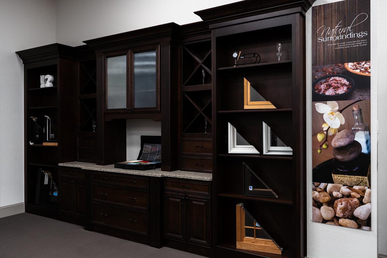 Dark wood cabinets with sample frames and decor, featuring Builders FirstSource materials and a "Natural Surroundings" banner.