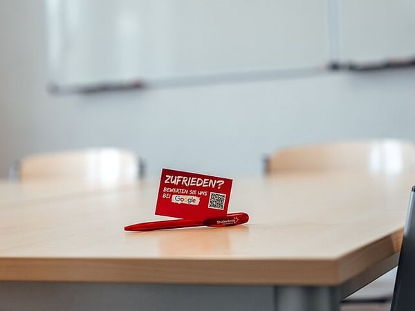 Beispiel Unterrichtsraum vor Ort mit Tisch, Stühlen und White Board an der Wand.