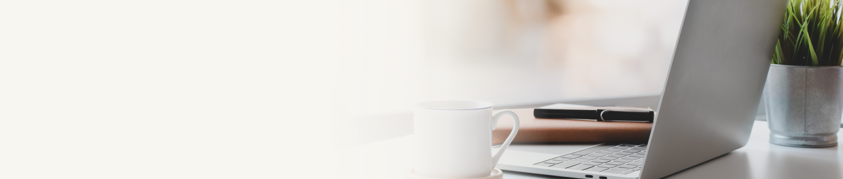 An open laptop, notebook, pen, and mug on a desk.