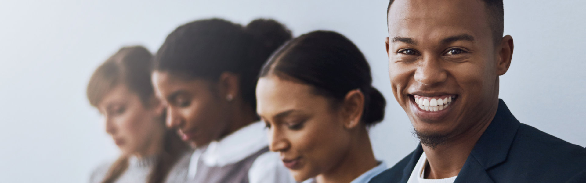 A diverse group of four young adults, likely applicants, stand in a line against a neutral backgroun 