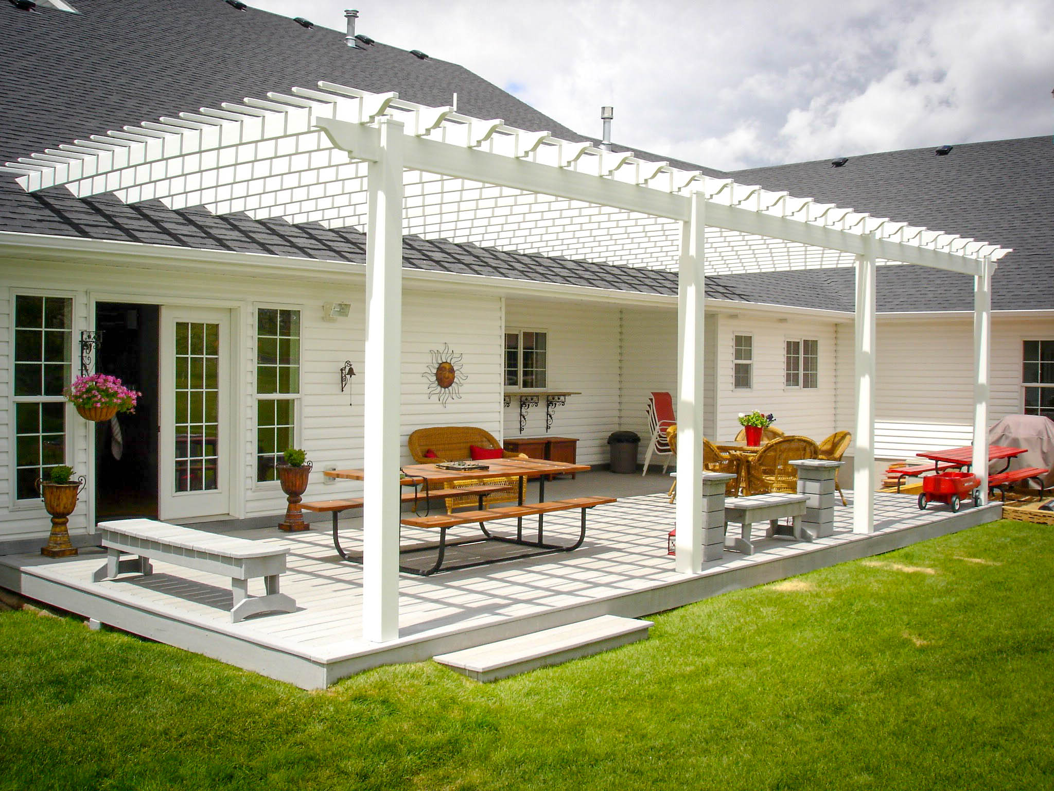 Create a charming and shaded backyard retreat with a custom vinyl pergola from DeckPro LLC. This project in Rexburg, Idaho, features an attached pergola design that provides filtered shade over the patio. The installation includes a matching white vinyl railing system with integrated flower boxes, combining beauty, function, and maintenance-free durability for the ultimate outdoor living space.