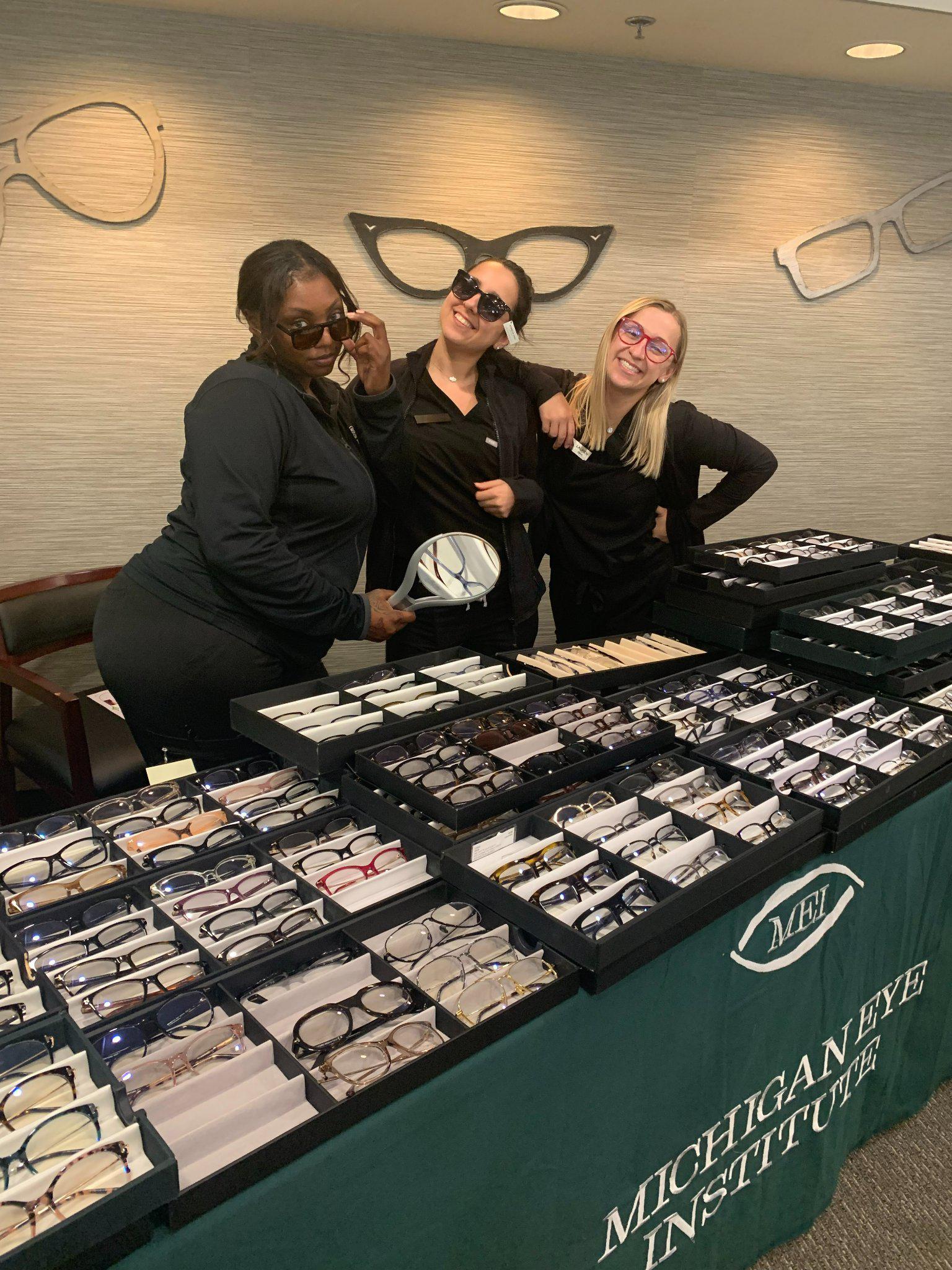 Michigan Eye Institute Employees standing behind a pop-up table displaying different styles of glasses and lenses.