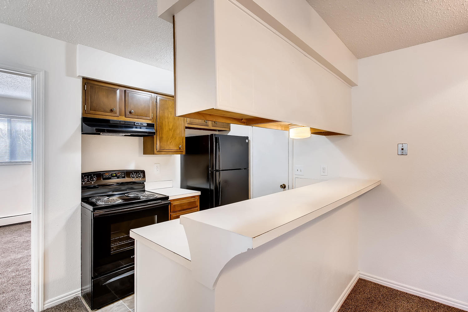 Breakfast bar with view to kitchen with black appliances and cherry wood cabinets.