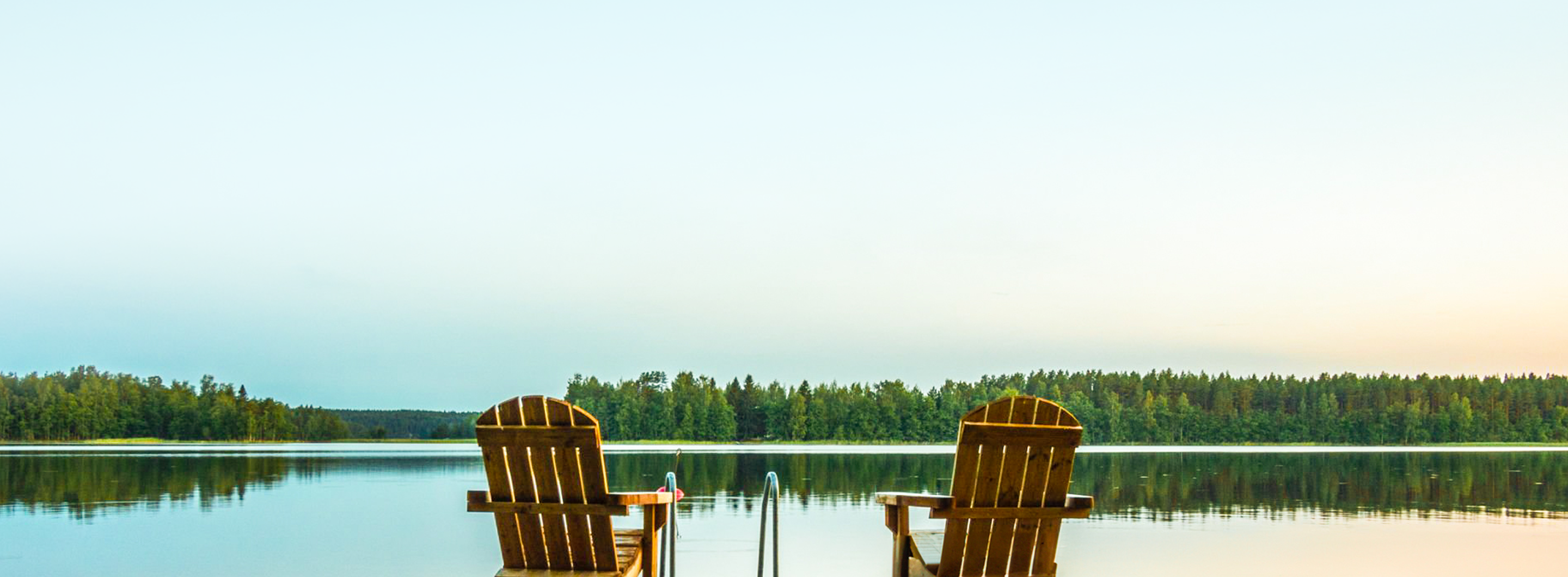 Two Muskoka chairs on a dock facing a calm lake.