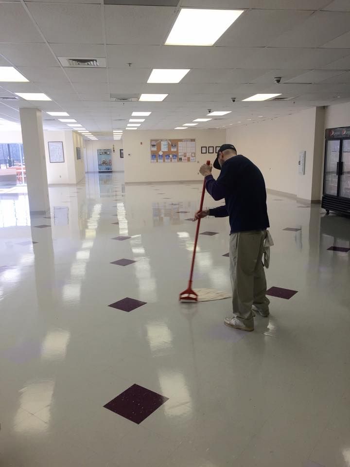Janitorial worker mopping large commercial floor in open indoor space, maintaining cleanliness and shine across polished surface, demonstrating routine cleaning services in a bright, high-traffic facility environment.