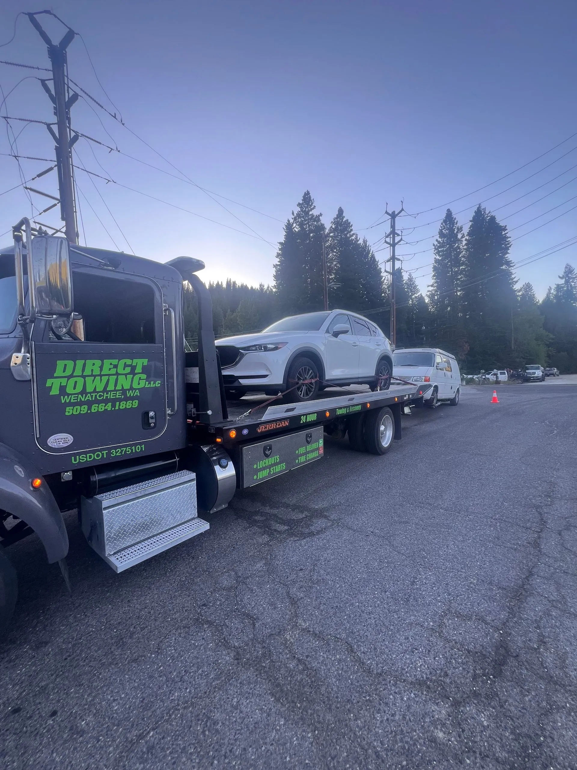 Direct Towing flatbed transporting a white SUV while roadside support vehicles remain nearby, showcasing professional recovery operations, secure loading procedures, emergency assistance, and dependable towing services.