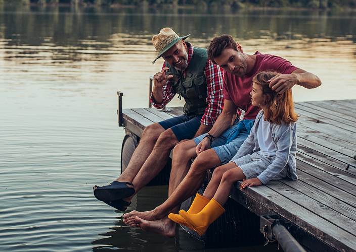 Two adults and a young child sitting together on the edge of a dock.