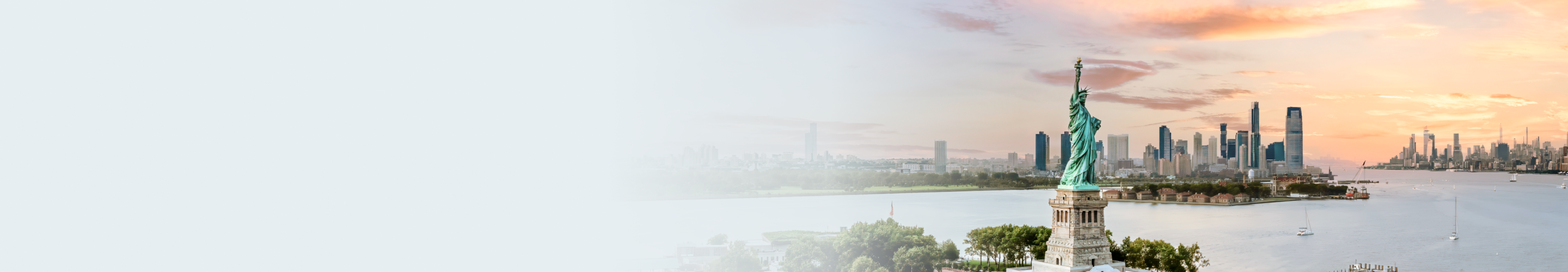 The Statue of Liberty in the foreground with New York Harbour and the city skyline in the background at sunset.