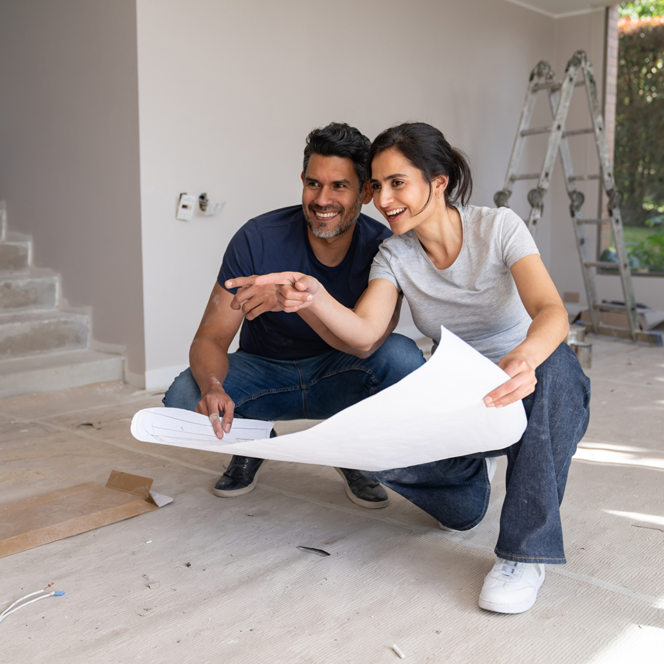 Two people crouching looking at building plans.