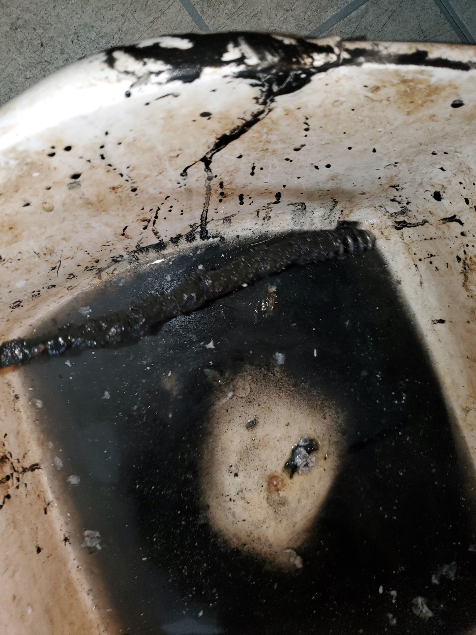 A heavily stained sink filled with dark, dirty water and debris, with a drain auger partially visible, showing a severe clog and buildup requiring urgent professional drain cleaning service.