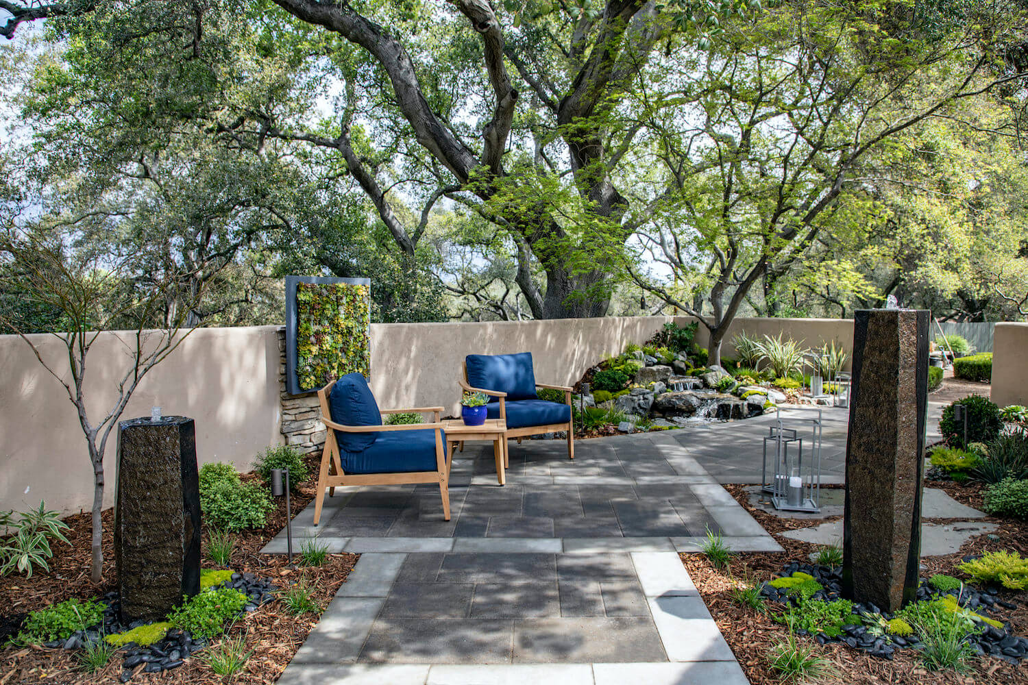 Serene landscaped courtyard with blue lounge chairs, stone path, water feature, garden walls, and mature trees creating a peaceful retreat.