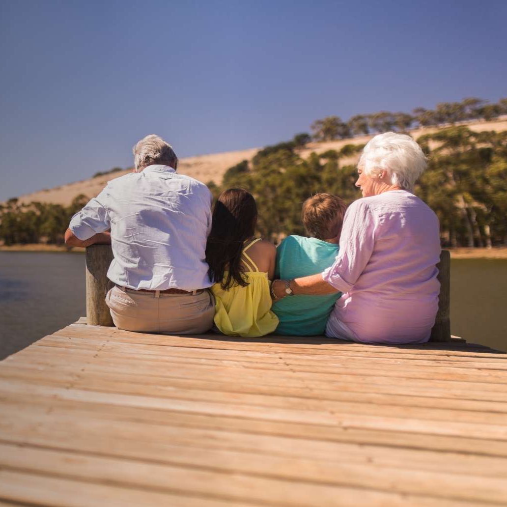 Two children and their grandparents sitting on a wooden dock.