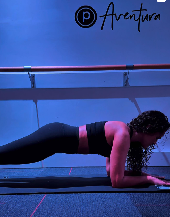 ure Barre Aventura studio — member holding a plank position during class with the ballet barre and Pure Barre Aventura branding visible