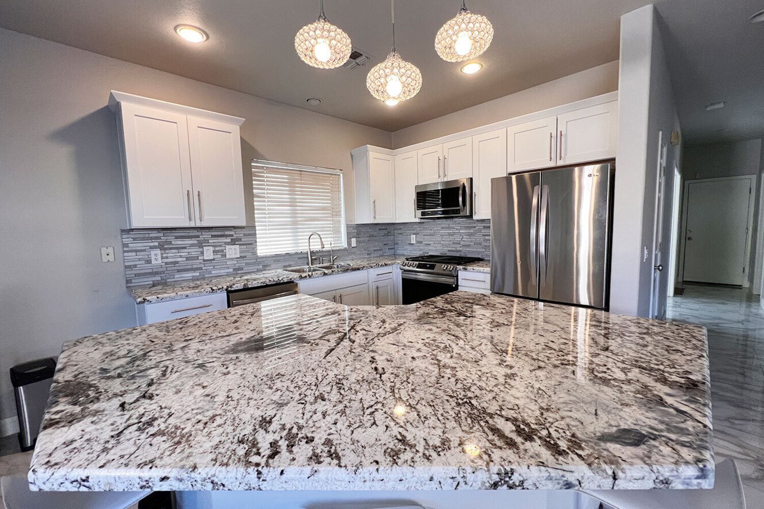 Completed kitchen remodel featuring white cabinetry, a large stone countertop, stainless steel appli 