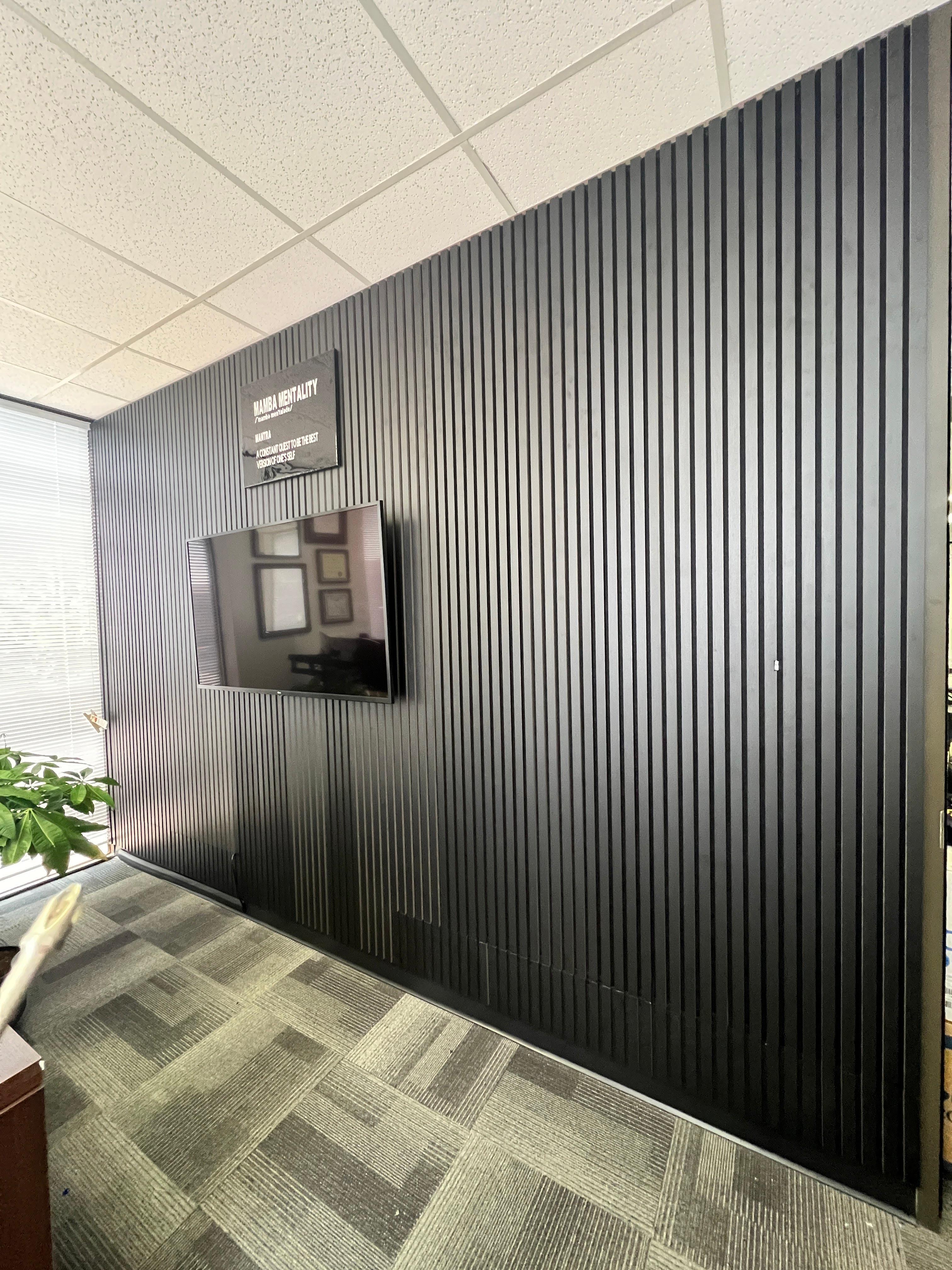 Wall-mounted TV installed on a black slat accent wall inside a commercial office in Houston, Texas.