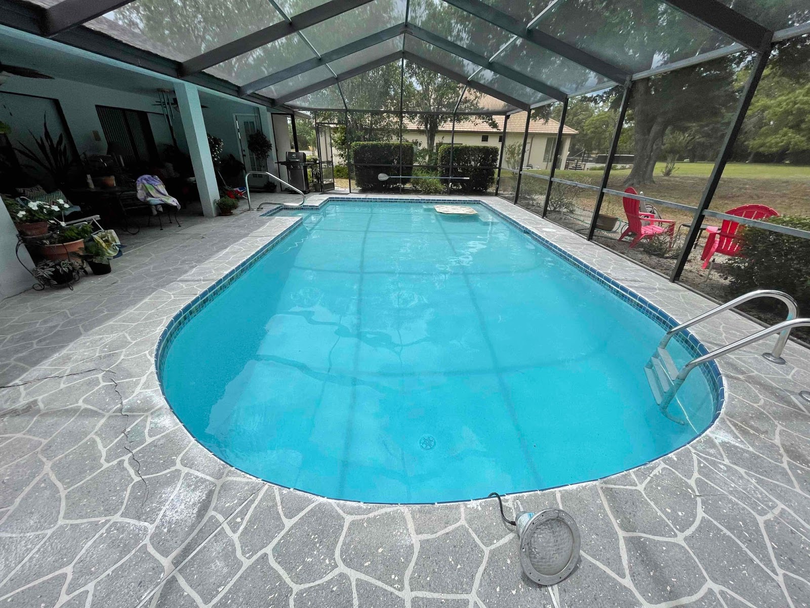 Screen-enclosed residential swimming pool with bright blue water, rounded corners, decorative stone decking, and a covered patio area.