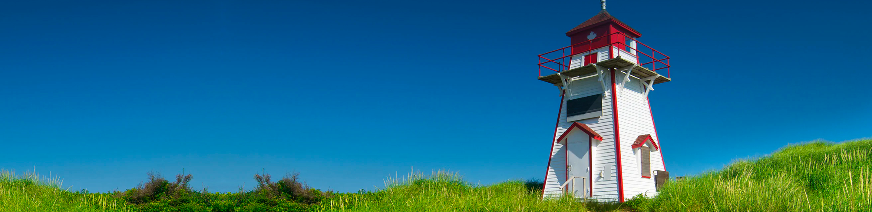 Red and white lighthouse on a grassy plain against a bright blue sky.