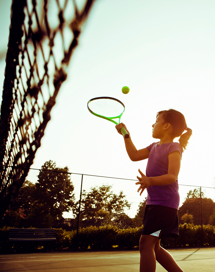 Young girl playing tennis on a sunny day.