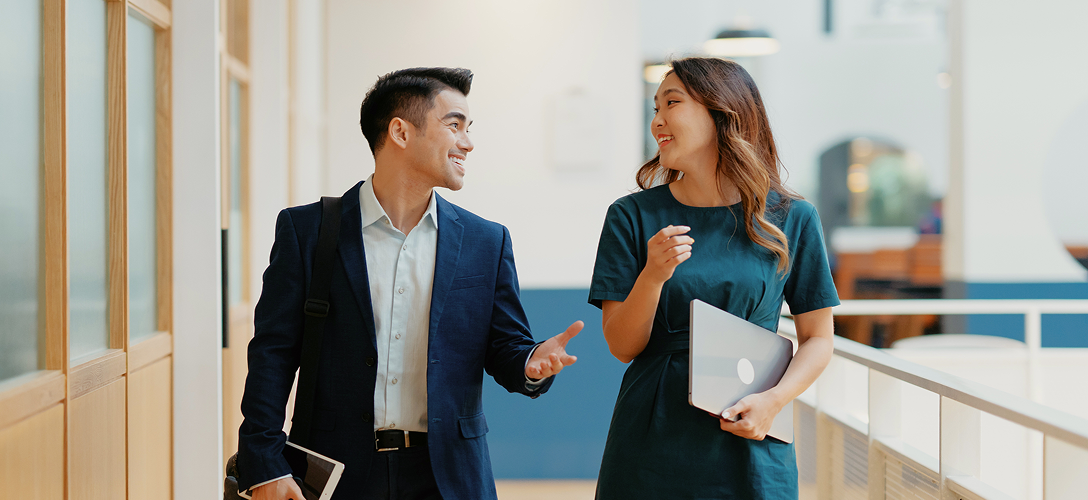 Two professionals walking and talking in an office.