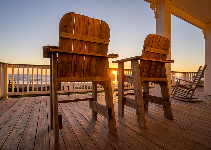 Wooden chairs on a beach-front deck during sunset.
