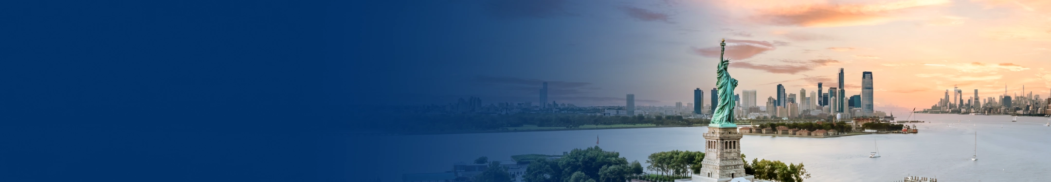 The Statue of Liberty in the foreground with New York Harbour and the city skyline in the background at sunset.