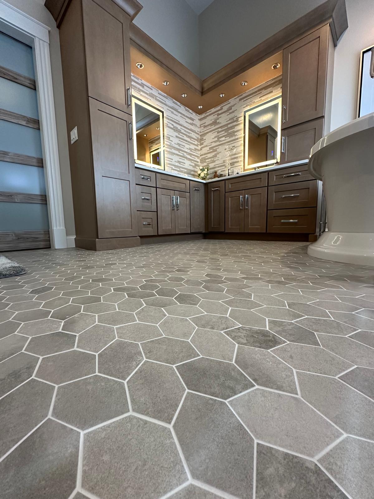 Custom bathroom remodel featuring natural stone hexagon tile flooring and rich dark wood cabinetry. This luxury upgrade combines high-end finishes with expert craftsmanship. The unique stone tile pattern adds texture and visual interest, while the custom vanity with double sinks and backlit mirrors creates a warm, spa-like atmosphere. Every detail was executed with precision to deliver a durable, elegant space our clients love. Quality work by V Morais Construction.