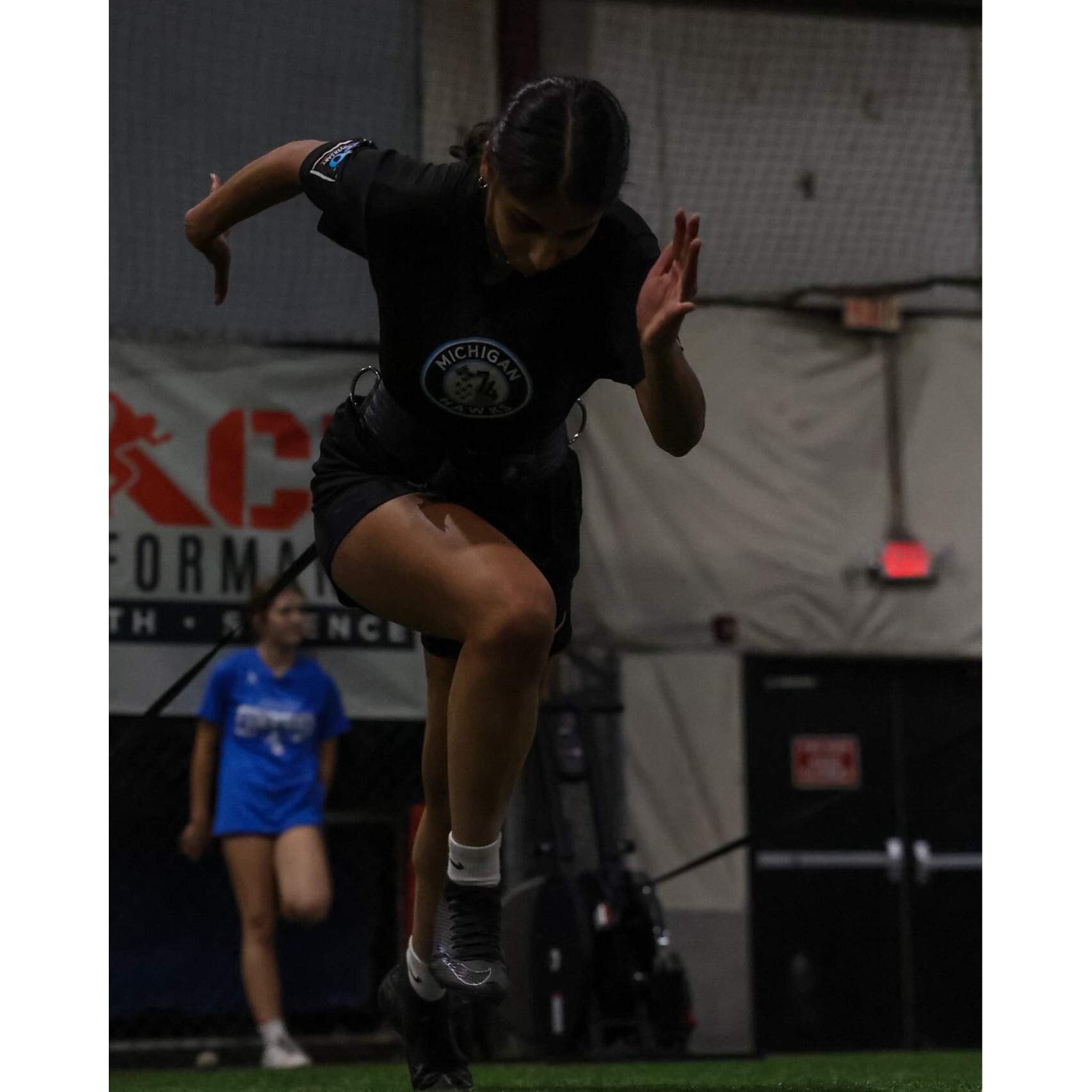 Female athlete performing band-resisted speed drill on turf at Impact Sports Performance